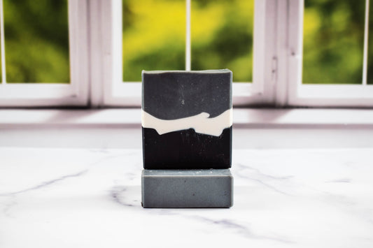 Black and white soap bar on a white surface with a blurred green and white background