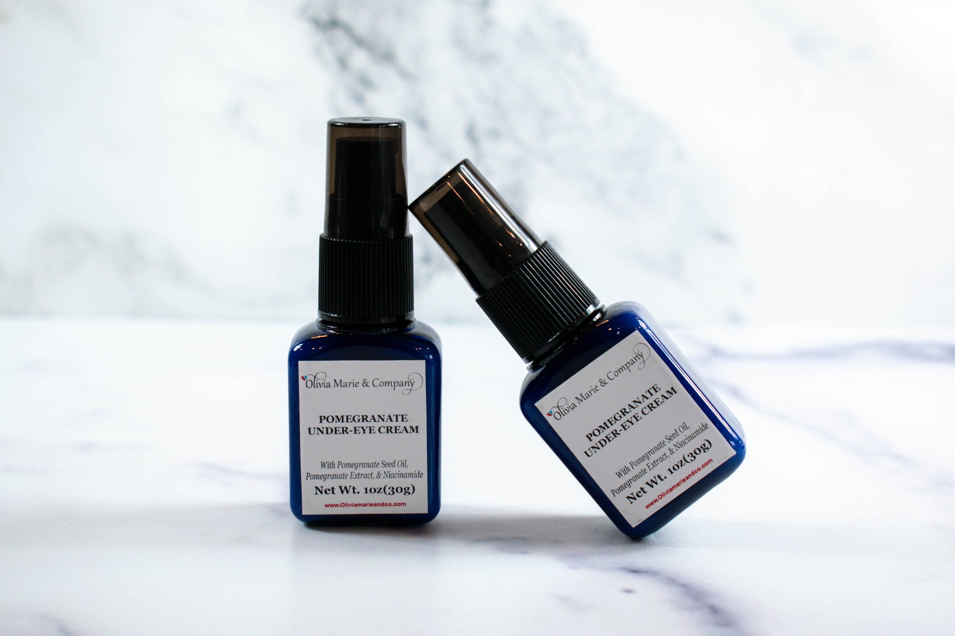 Two bottles of under-eye cream with pumps, one standing upright and the other lying down, on a marble surface.