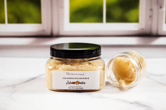 Jar of cleansing sugar scrub with a black lid on a white surface, with a blurred window background.