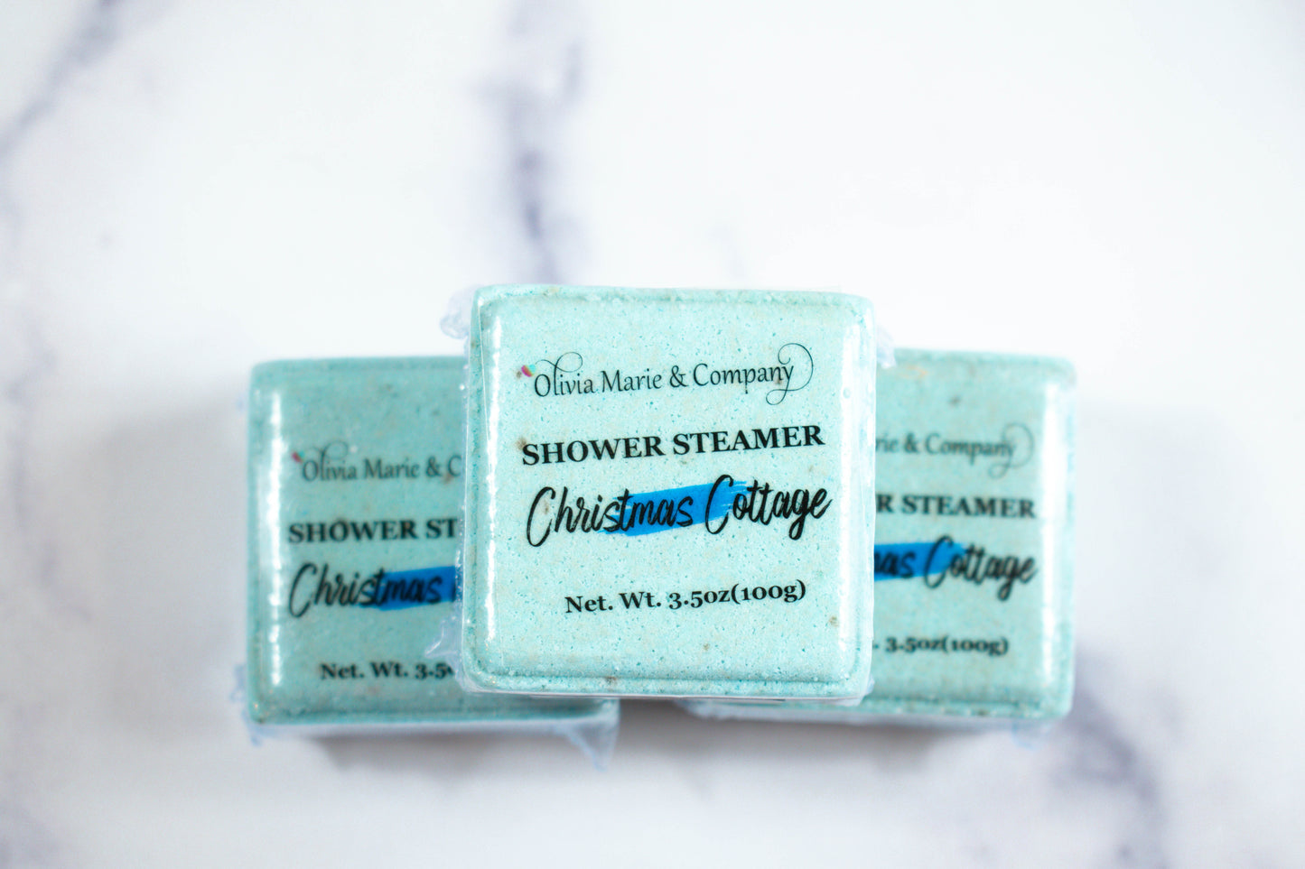 Three blue shower steamers labeled 'Christmas Cottage' by Olivia Marie & Company on a white background.