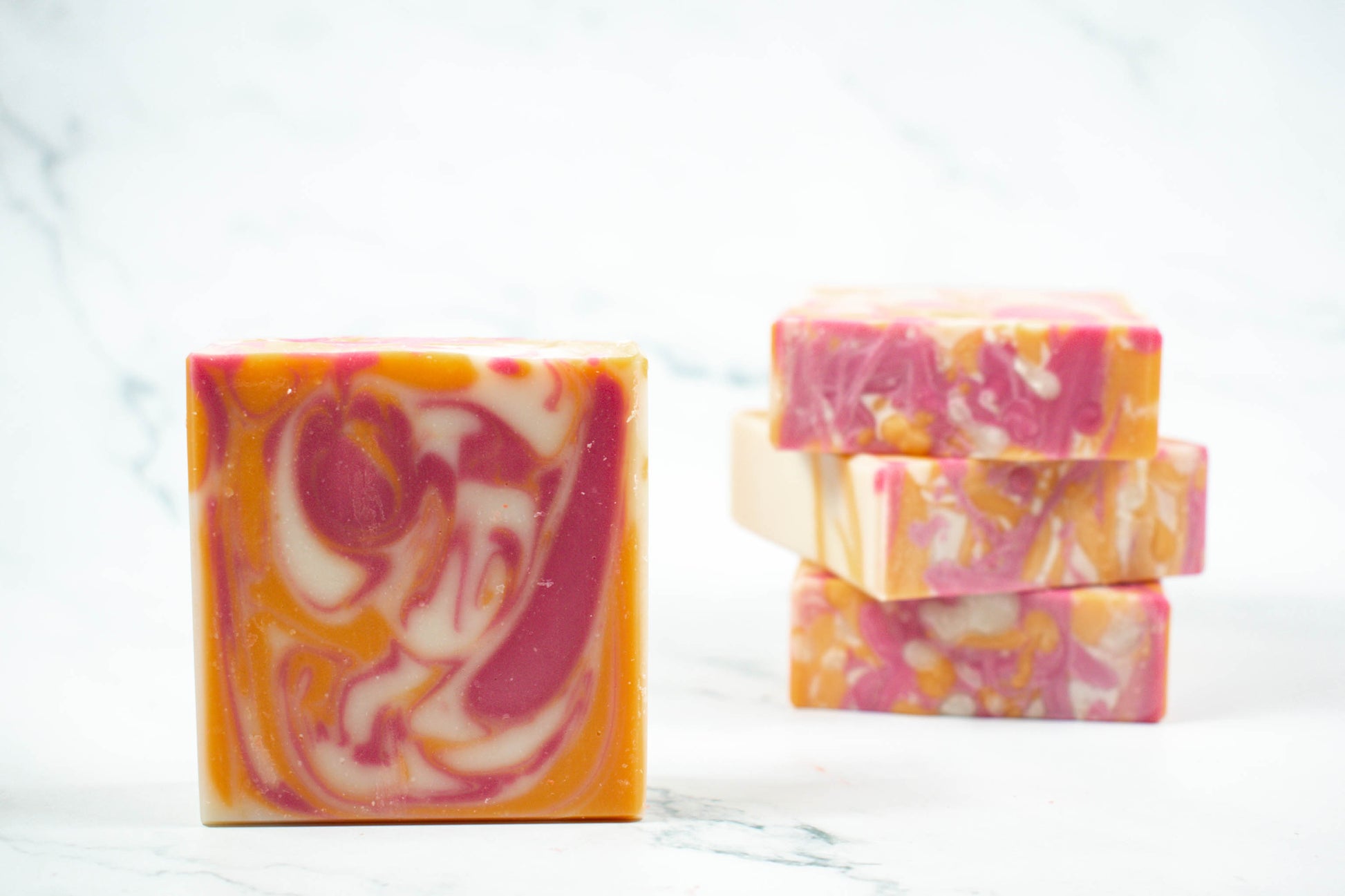 Orange, pink, and white swirls in the soap with 1 in front and 3 soaps in the back.